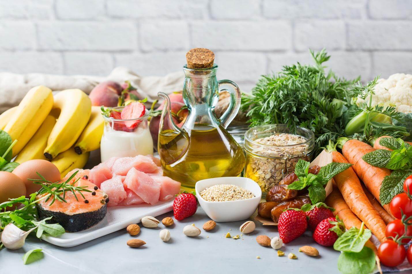 Mesa con alimentos de un patrón mediterráneo: salmón, pollo, huevos, aceite de oliva, avena, frutos secos, fruta y verdura fresca