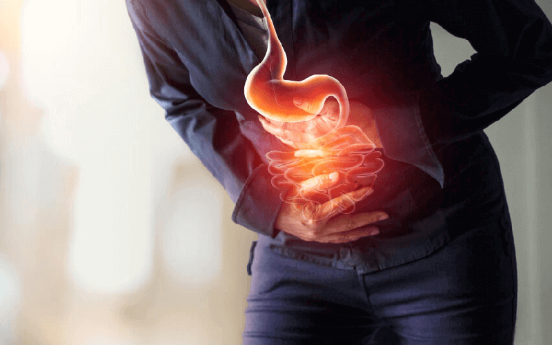 ¿La creatina te sienta mal? Por qué da diarrea y cómo evitarlo 1 Persona con la mano en el abdomen y una ilustración del estómago e intestino superpuesta